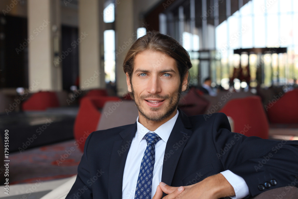 Portrait of happy young businessman sitting on sofa in hotel lobby. Portrait of happy young businessman sitting on sofa in hotel lobby.