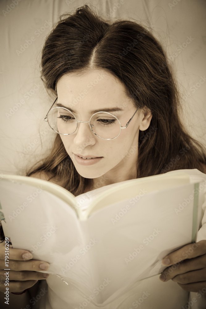 Girl reading a book in bed, lying on her stomach smiling happy and relaxed on a leisure day at home.