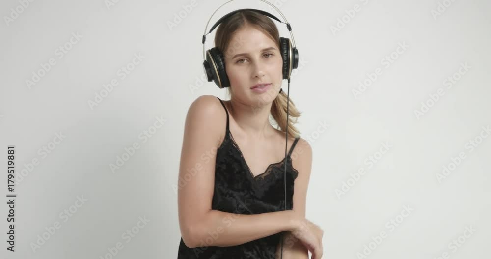Blond young woman in headphones and black lacy camisole listening to music in headphones and dancing