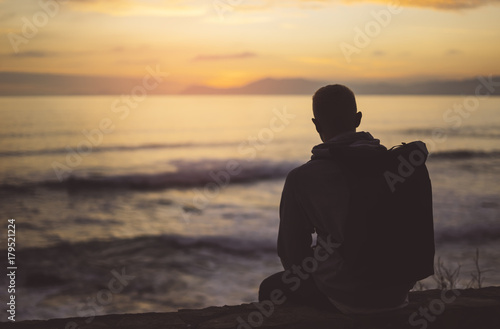Hipster hiker tourist with backpack looking seascape sunset on background sea, guy enjoying ocean horizon panoramic sunrise, traveler relax holiday concept, sunlight view in trip vacation