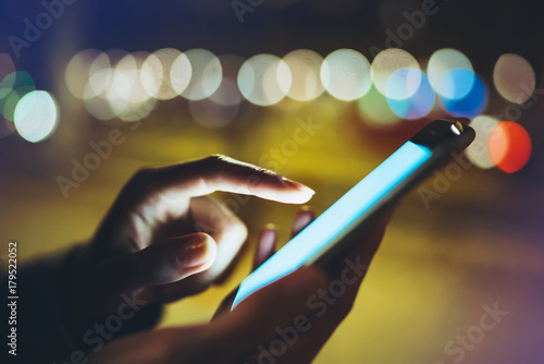 Woman pointing finger on screen smartphone on background illumination bokeh light in night atmospheric city, hipster using in hands mobile phone closeup, mockup street, online wifi internet concept