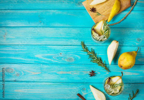 Pear cocktail with rum, liquor, pear slices and rosemary on an blue wooden table, selective focus