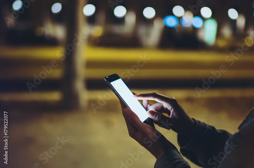 Woman pointing finger on screen smartphone on background illumination bokeh light in night atmospheric city, hipster using in hands mobile phone closeup, mockup street, online wifi internet concept
