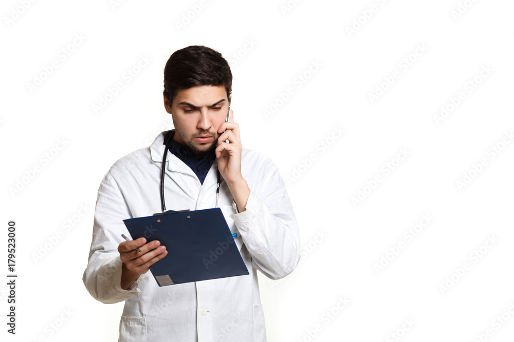 beautiful young doctor in a dressing gown with a stethoscope on a white background in the studio, records a medical history, talking on the phone beautiful young doctor in a dressing gown with a stethoscope on a white background in the studio, records a medical history, talking on the phone
