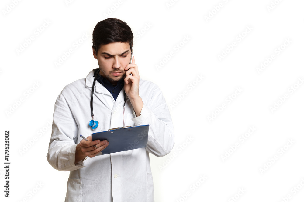 beautiful young doctor in a dressing gown with a stethoscope on a white background in the studio, records a medical history, talking on the phone beautiful young doctor in a dressing gown with a stethoscope on a white background in the studio, records a medical history, talking on the phone