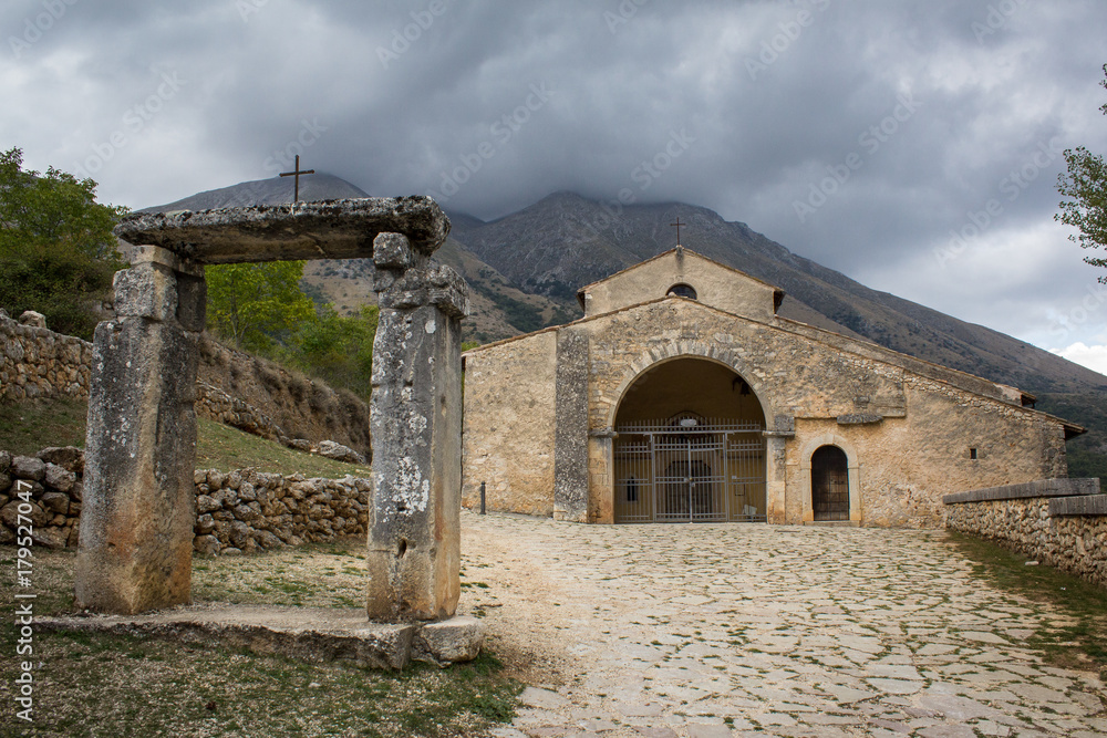 Santa Maria in Val Porclaneta Church, under Velino Mountain , under a cloudy sky. Magliano dei Marsi, Rosciolo, Abruzzo, Italy. 