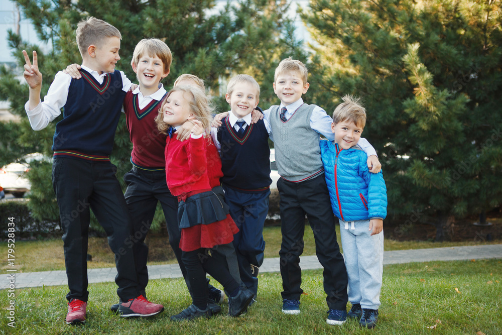 Happy school children in uniform and with backpacks holding hands and jumping in the park, back to school Happy school children in uniform and with backpacks holding hands and jumping in the park, back to school