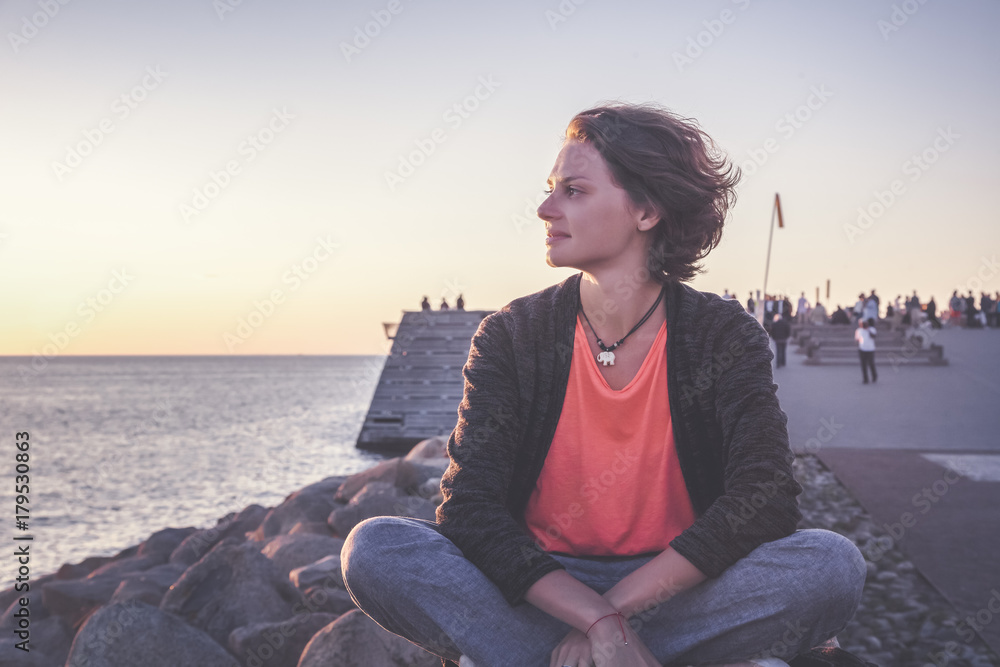Beautiful young woman sitting on the beach watching the sunset