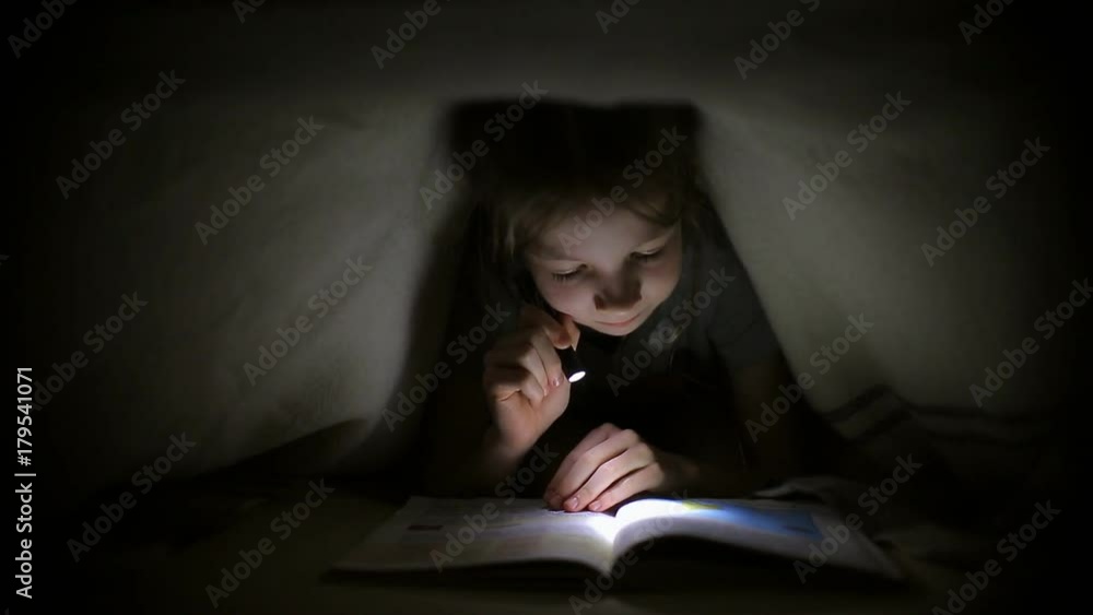 little girl is reading a book under a blanket with a flashlight in a dark room at night little girl is reading a book under a blanket with a flashlight in a dark room at night