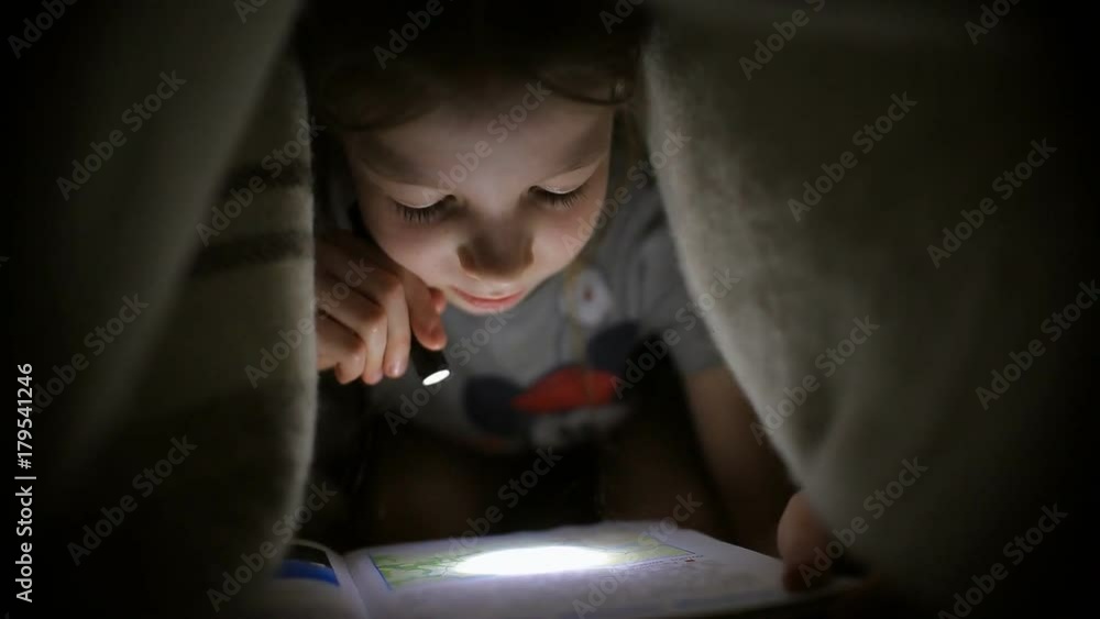 little girl is reading a book under a blanket with a flashlight in a dark room at night little girl is reading a book under a blanket with a flashlight in a dark room at night