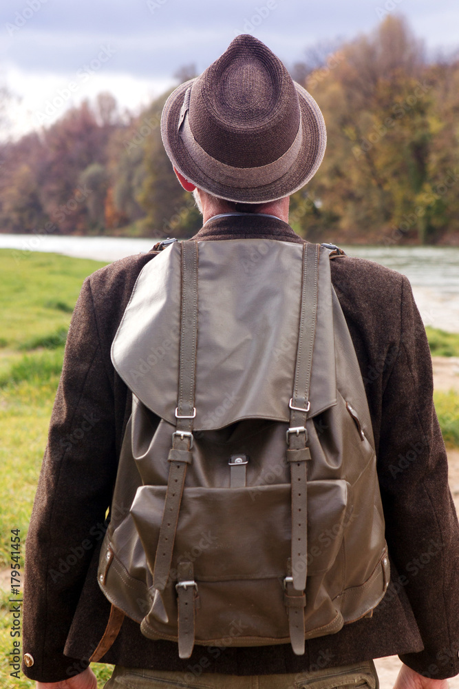 backside of bavarian man with backpack standing by river backside of bavarian man with backpack standing by river