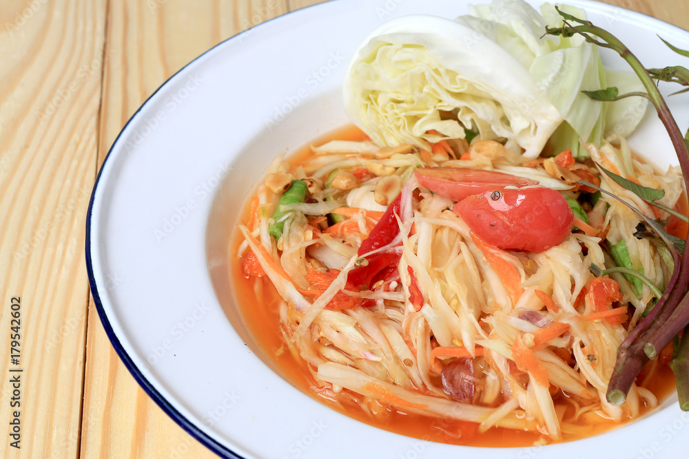 Papaya Salad with Carrot, Lentils, Tomato, Dried Shrimp, Chilli, in a White plate on wooden background. Thai style food.