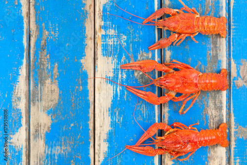 Row of three whole red boiled crawfish on old rustic blue wooden planks