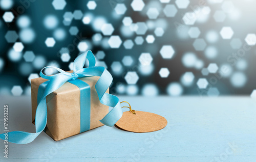 Christmas gift or New Year with blue ribbon and greeting card on wood table on bokeh background. Tiny and Handmade gift box concept.