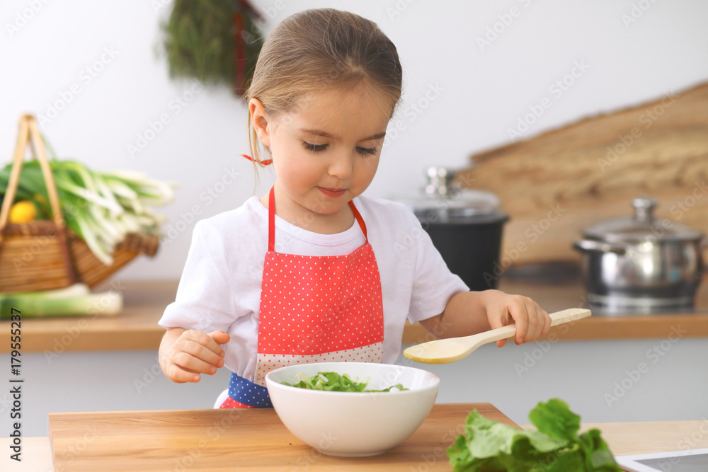 Little girl cooking in the kitchen. Kid slicing and mixing tomatoes and greenery. Concept of healthy meal or tasty breakfast Little girl cooking in the kitchen. Kid slicing and mixing tomatoes and greenery. Concept of healthy meal or tasty breakfast