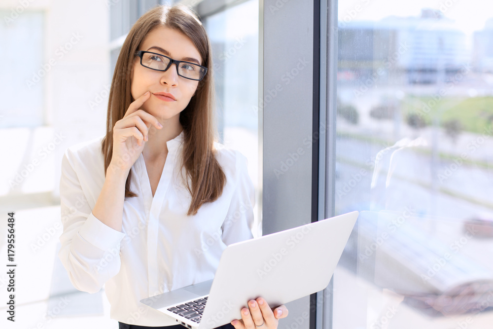 Modern business woman typing on laptop computer while standing in the office before meeting or presentation Modern business woman typing on laptop computer while standing in the office before meeting or presentation
