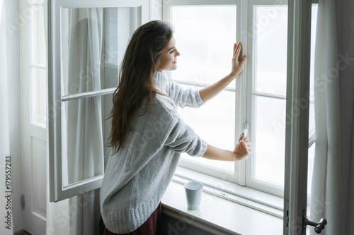 Woman in warm woolen pullover is opening window photo