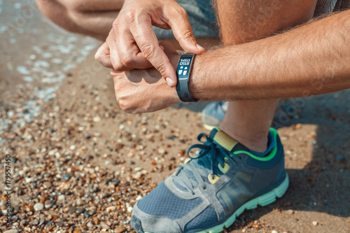 male athlete checking step count in smart wristband at the seashore in summer