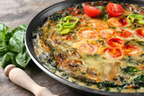 Frying pan with delicious spinach frittata on table, closeup