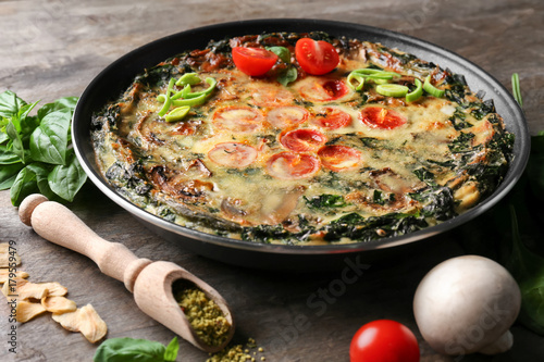 Frying pan with delicious spinach frittata on wooden background