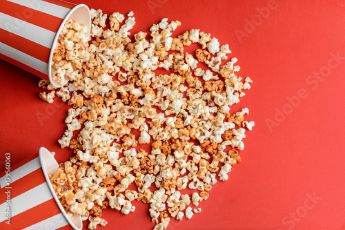 Overturned cups with tasty caramel popcorn on color background
