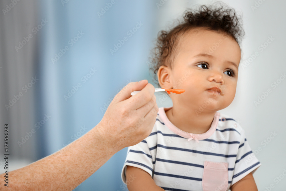 Mother feeding baby with spoon indoors Mother feeding baby with spoon indoors