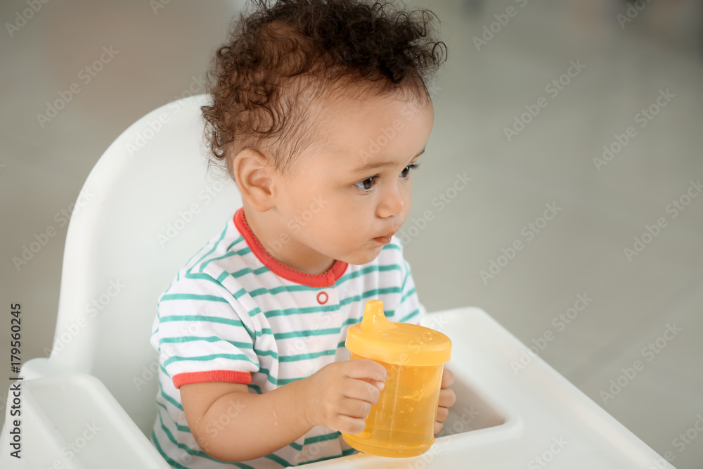 Cute baby with bottle of water sitting on chair indoors Cute baby with bottle of water sitting on chair indoors