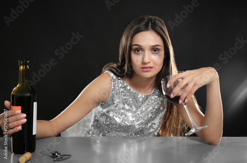 Young woman drinking alcohol at table against black background