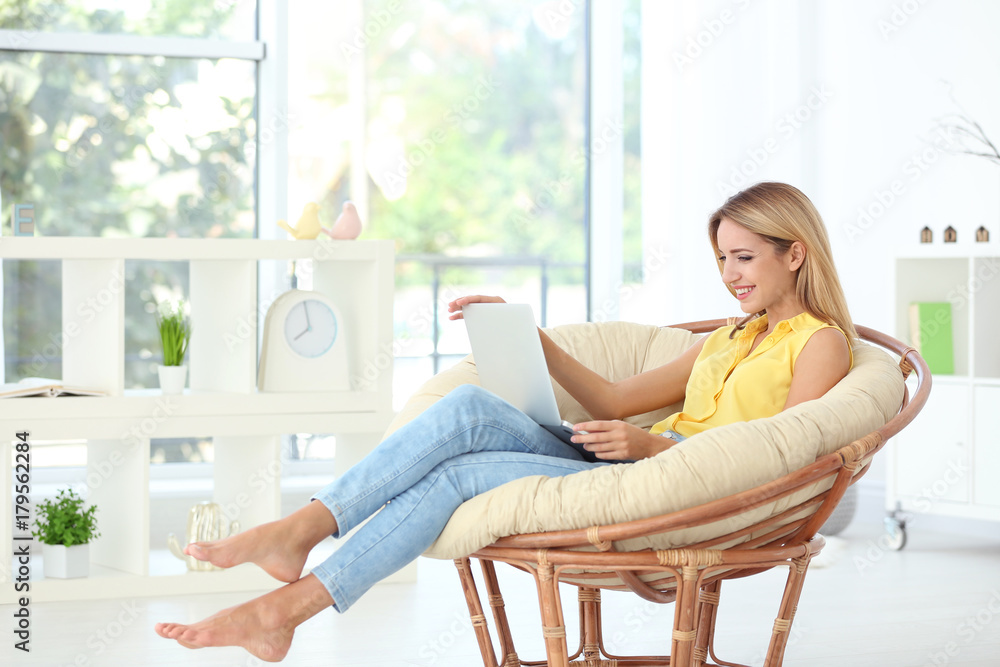 Beautiful young woman with modern laptop in armchair at home Beautiful young woman with modern laptop in armchair at home