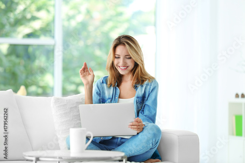 Beautiful young woman with modern laptop on sofa at home