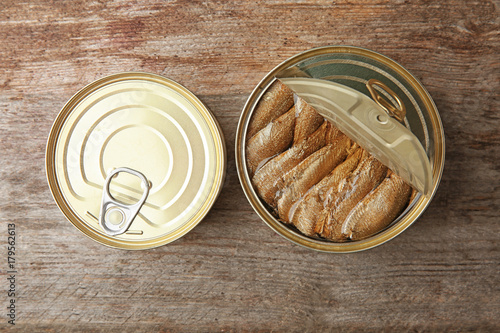 Open and closed tin cans with fish on wooden background