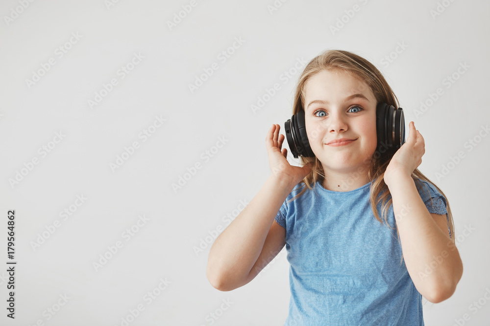 Funny cheerful girl with light hair and blue eyes, wearing headphones. looking in camera with shocked expression after loud music suddenly starts to play Funny cheerful girl with light hair and blue eyes, wearing headphones. looking in camera with shocked expression after loud music suddenly starts to play