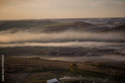 An aerial photograph of a village near a forest on which the fog falls