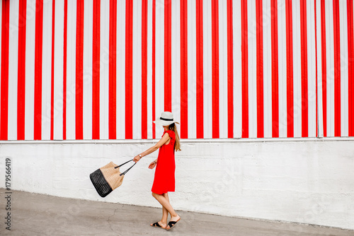 Young woman in red dress on the striped wall background. Wide geometrical view with copy space