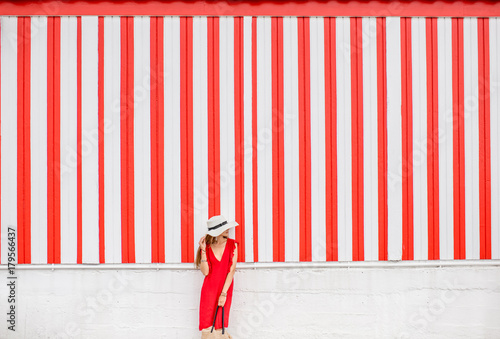 Young woman in red dress on the striped wall background. Wide geometrical view with copy space