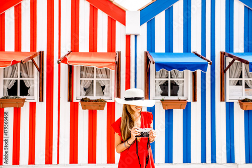 Young woman in red dress and sun hat standing on the colorful striped houses background