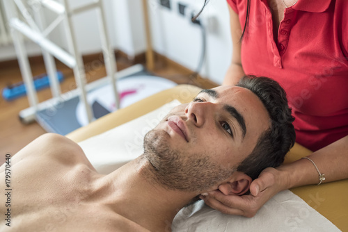 fisioterapista massaggia giovane paziente per curare un dolore cervicale photo