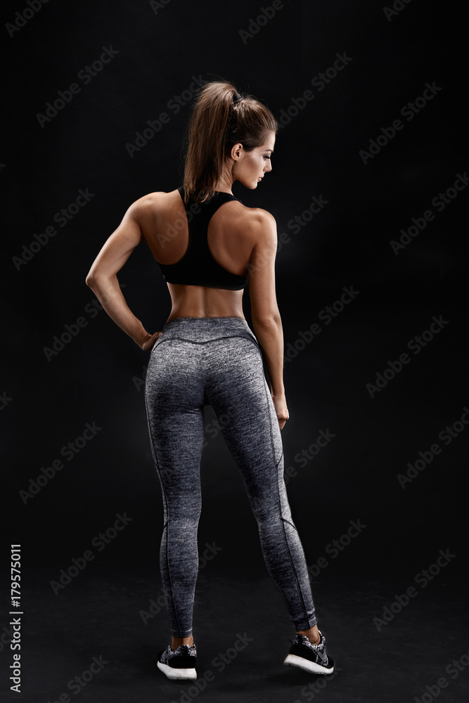 Shot of a strong woman with muscular abdomen in sportswear. Fitness female model posing on black background. Shot of a strong woman with muscular abdomen in sportswear. Fitness female model posing on black background.