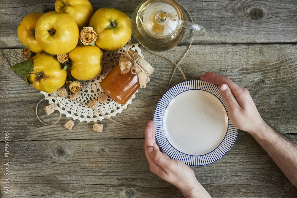 masculine hands holding empty plate with jar of jam and quinces on rustic wooden background