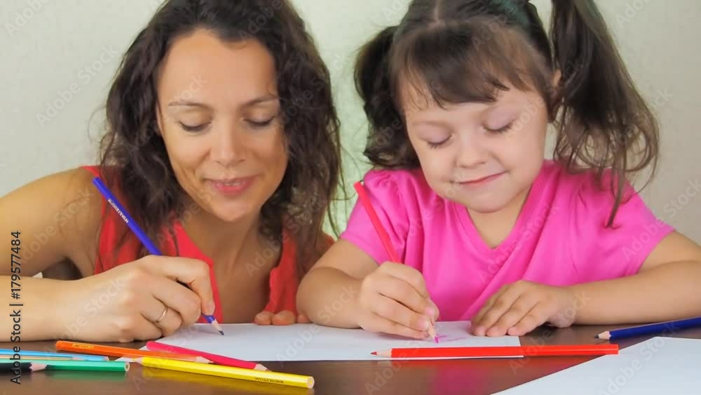 The child with his mother draws in colored pencils. Mom teaches a little daughter to draw. The child with his mother draws in colored pencils. Mom teaches a little daughter to draw.