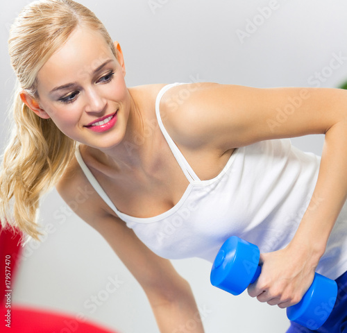 Young happy smiling woman with dumbbells, indoors