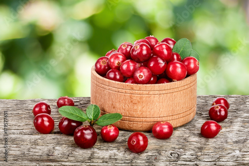 Cranberry with leaf in wooden bowl on old wooden table with a blurry garden background
