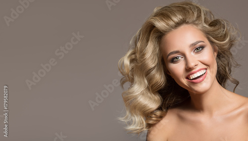 Blonde woman with curly beautiful hair smiling on gray background.
