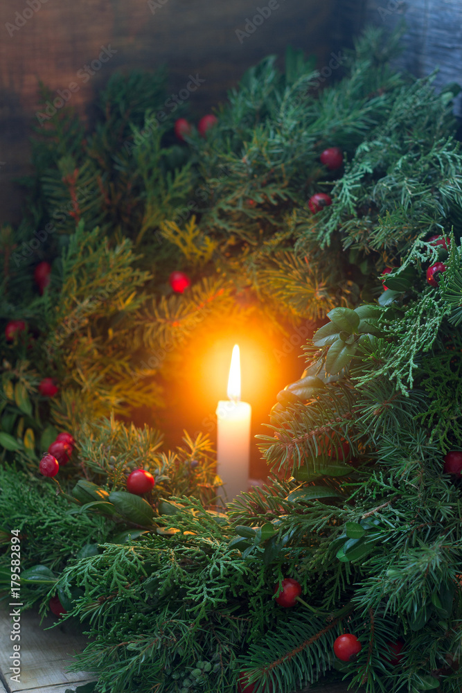 A Christmas wreath made of fir branches, juniper, tuja, boxwood and wild rose berries. Wreath with burning candles.
