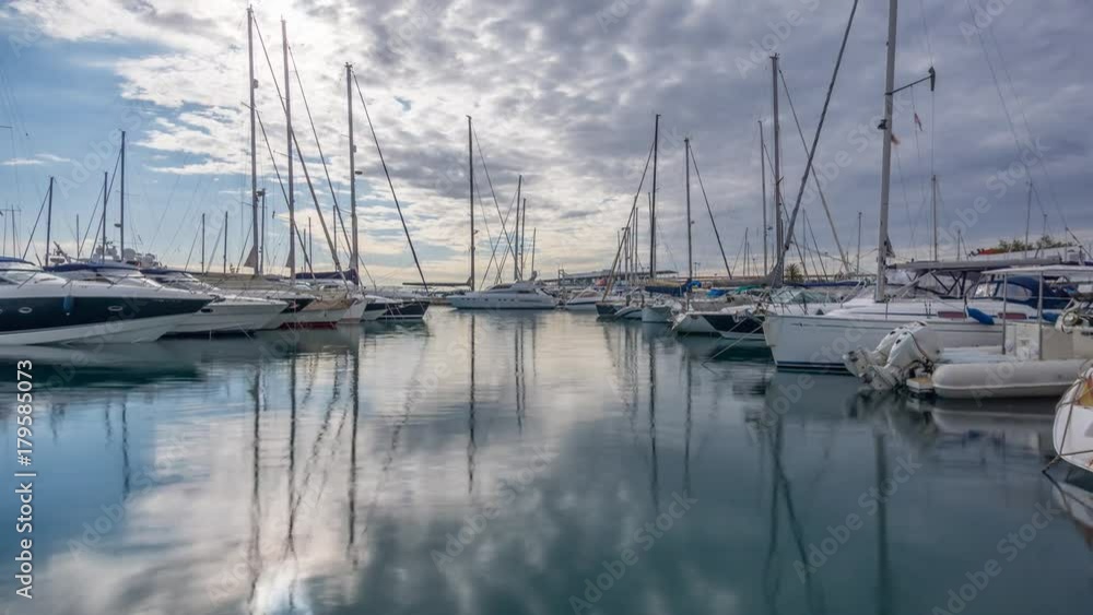 sailboats in a marina, moored. Reflection in the mirrored water passing clouds sailboats in a marina, moored. Reflection in the mirrored water passing clouds