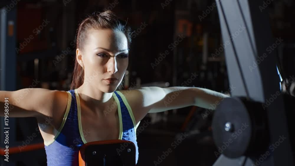 Attractive female athlete doing workout and training hands and chest on weights exercise machine in gym Attractive female athlete doing workout and training hands and chest on weights exercise machine in gym