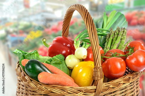 Green Grocery shopping concept image - basket full of varied fresh vegetables on a blurred supermarket background.