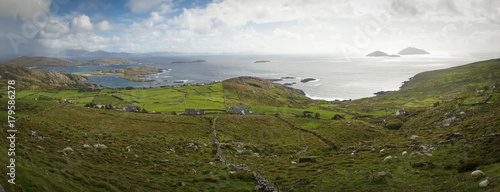 Vue panoramique dans le comté de l'anneau du Kerry. A l'horizon, la mer et des îlots. Au premier plan, des maisons et champs verdoyants avec murets de pierres et des moutons. 