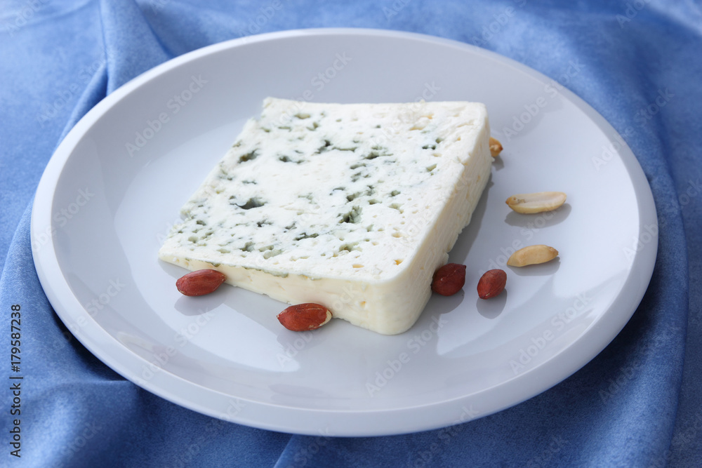Cheese with mold and nuts on a white plate, sheep cheese on a blue background, cheese and peanut white plate on a blue napkin, cheese and walnut in a minimalist style, retro style