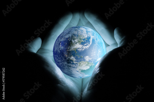 Men's hands holding the planet earth rotated the continents of North and South America with a blue glow on a black background.